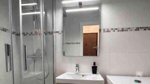 Ein Badezimmer mit einer Glaskabine zur Dusche, einem Waschbecken mit Spiegel darüber und einer Waschmaschine.