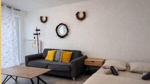 Ein modernes Wohnzimmer mit einer Couch, einem Couchtisch und einem Bett. Es sind Wanddekorationen und ein Heizkörper zu sehen.