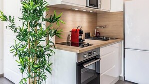 A compact kitchen with a built-in stove, oven, and microwave, a sink, and a potted plant. - Chez Hubert | Proche Genève I Beaumont (Beaumont)