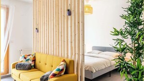 A modern room with a yellow sofa, a bed, a wooden partition, and a potted plant. - Chez Hubert | Proche Genève I Beaumont (Beaumont)
