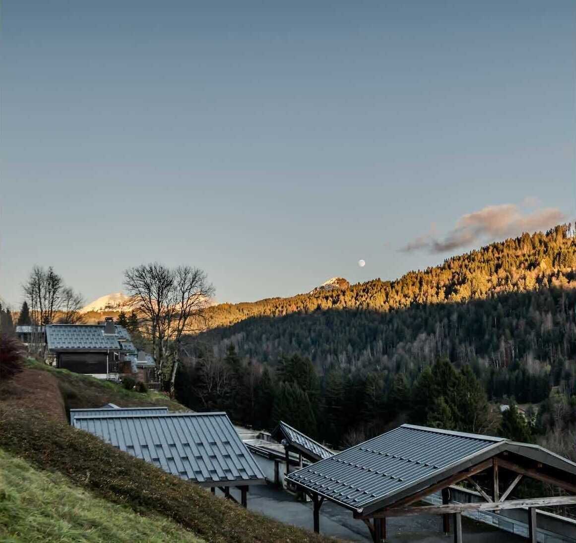 Landelijk tafereel met heldere lucht, een berg op de achtergrond en meerdere gebouwen met schuine daken.