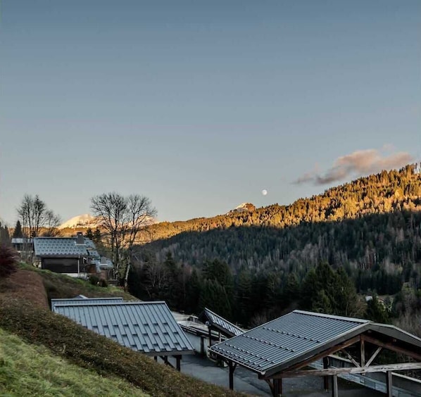 A rural setting with a clear sky, a mountain in the background, and several buildings with sloped roofs.