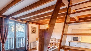 Interior acogedor de una cabaña con techo de madera, un sofá, zona de comedor y cocina.