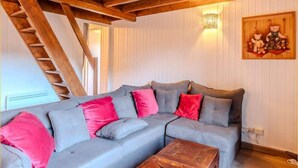 Una sala de estar acogedora con un sofá seccional gris, vigas de madera, una mesa de centro de madera y una escalera.