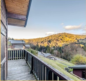 A wooden deck with a view of a forested mountain and a small building in the distance.