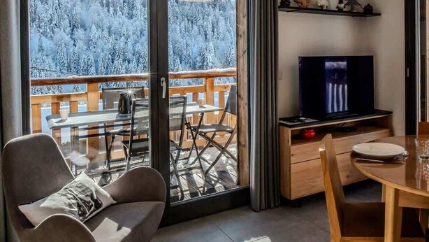 A modern room with a balcony, a TV, and a dining area. - L'évasion I T3 I Les Gets (Les Gets)