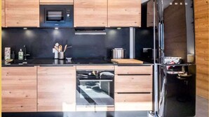 A modern kitchen with wooden cabinets, a black refrigerator, a microwave, and a dishwasher. - L'évasion I T3 I Les Gets (Les Gets)