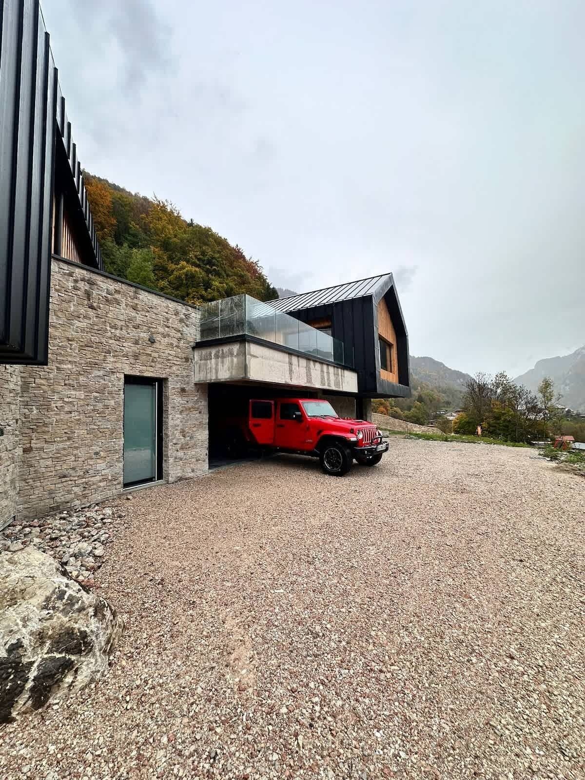 Un edificio moderno con un camino de grava y un vehículo rojo estacionado en el garaje.