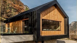 Eine moderne Holzhütte mit großen Fenstern, gelegen an einem felsigen Hang.