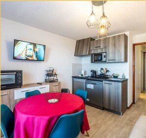 Eine kompakte Küche mit Mikrowelle, Kaffeemaschine und Spüle. Ein Esstisch mit Stühlen und ein an der Wand befestigter Fernseher sind vorhanden.