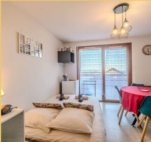 Ein gemütliches Schlafzimmer mit Bett, Nachttisch, Lampe und Blick nach draußen durch eine Schiebetür.