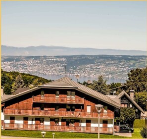 Un bâtiment de style chalet, doté de nombreux balcons, offrant une vue sur la ville et les montagnes en arrière-plan.