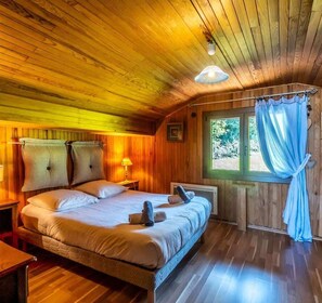 Ein Schlafzimmer einer Holzhütte mit einem Bett, Nachttischlampen und einem Fenster mit Vorhängen.