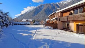 Rua coberta de neve com edifícios de um lado e montanhas ao fundo.