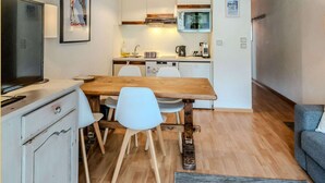 Uma cozinha compacta com vigas de madeira no teto, uma mesa de jantar com cadeiras, uma televisão e uma bancada de cozinha.