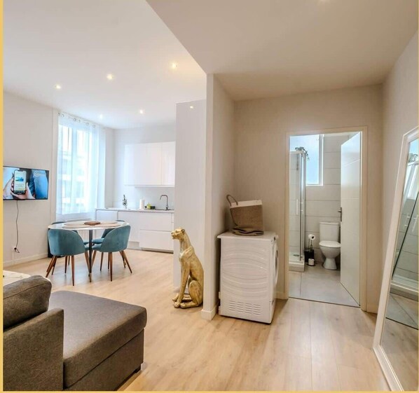 A modern living room with a sofa, a dining table with chairs, a kitchen area with cabinets, and a bathroom with a toilet and shower.
