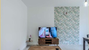 Una sala de estar moderna con un televisor de pantalla plana sobre un soporte de madera, una mesita auxiliar con una planta y un sofá verde.