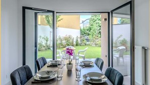 Comedor con una mesa preparada para cuatro personas, ventanas amplias y vista a un jardín.