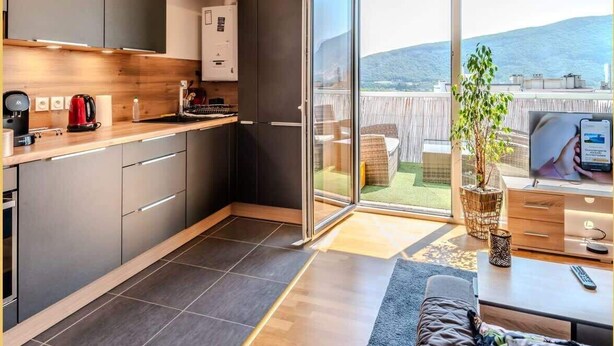 A modern kitchen with a built-in oven, a coffee machine, and a sliding glass door leading to a balcony with a view of the hills.