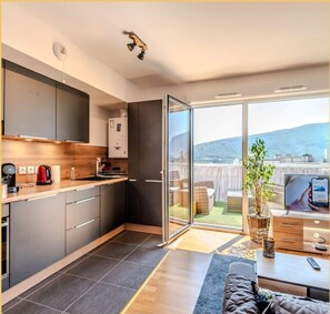 Una cocina moderna con horno integrado, cafetera y puerta de vidrio corredera que da a un balcón con vistas a las colinas.