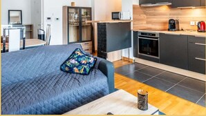 A compact hotel room with a bed, a small kitchenette, a dining area, and a bathroom.