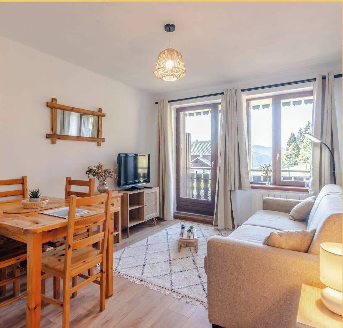 Un salon chaleureux avec une table à manger en bois, un canapé, un téléviseur et une grande fenêtre avec des rideaux.