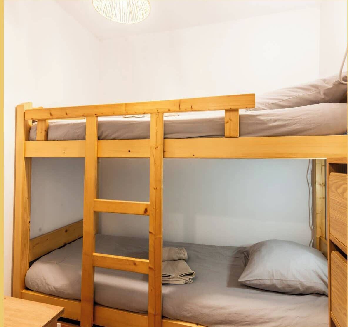 Un lit superposé avec une échelle, une literie grise et une tête de lit en bois.