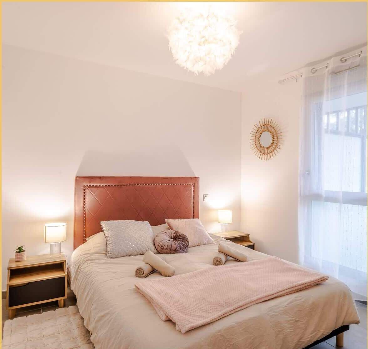 A bedroom with a large bed, two bedside tables, a chandelier, and a window with curtains.