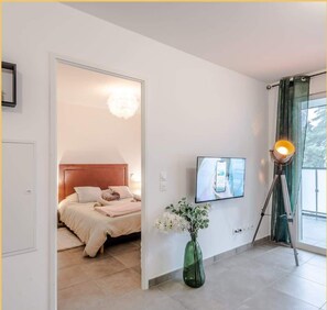A bedroom with a bed, a TV mounted on the wall, a floor lamp, and a vase with flowers. - Le 1848 I T2 I Cluses (Cluses)