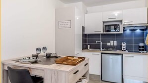 Cocina compacta con armarios blancos, microondas, lavavajillas y una mesa de comedor de madera con sillas.