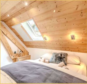 Een slaapkamer met een schuine kap, een dakvenster, een bed met kussens, een nachtkastje en een klein nachtkastje.