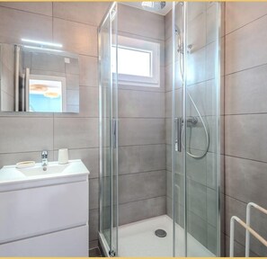 Ein modernes Badezimmer mit einer Duschkabine, einem Waschbecken mit Spiegel und einem Fenster für natürliches Licht.