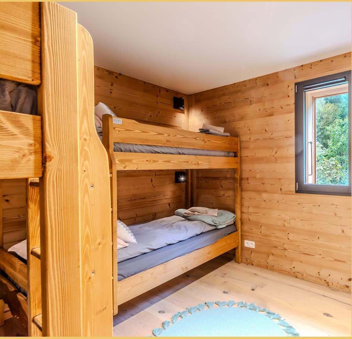 A bunk bed room with wooden walls and a window.