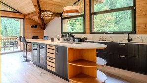 Eine moderne Küche mit Holzbalkendecke, großen Fenstern und einer zentralen Kochinsel.