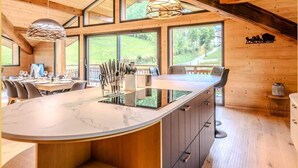 Eine moderne Küche mit einer großen Kochinsel, Holzbalken und großen Fenstern, die einen Blick ins Freie ermöglichen.