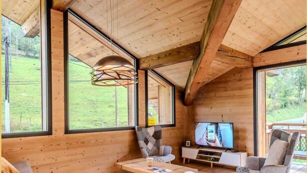 Ein modernes Blockhaus-Interieur mit großen Fenstern, einem Fernseher und einer gemütlichen Sitzecke.
