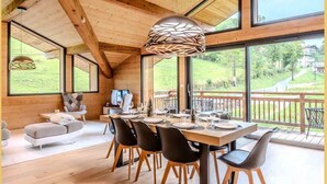 Ein geräumiger Essbereich mit Holztisch und -stühlen, großen Fenstern und Blick ins Freie.