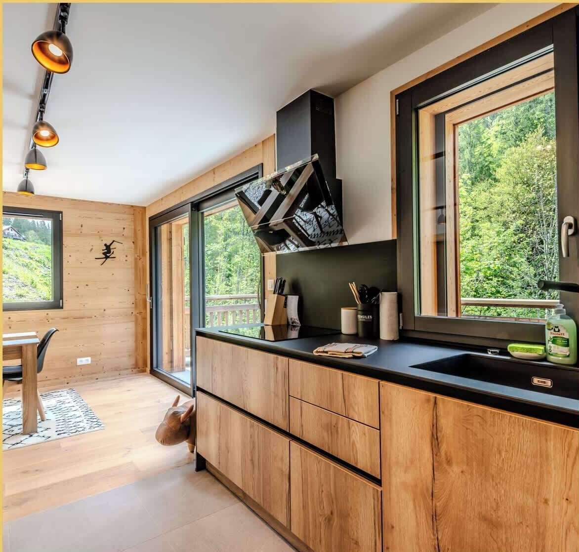 A modern kitchen with wooden cabinets, a black countertop, and a large window offering a view of greenery.