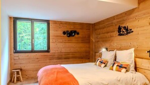 Camera da letto in una baita di legno, con un letto, una finestra e uno sgabello.