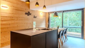 Una cucina moderna con isola centrale, parete in legno con insegna 'coffee bar', illuminazione a sospensione e un'ampia finestra che si affaccia su alberi.