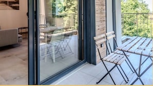 Un salon moderne doté d’une porte vitrée donnant sur un balcon, d’un mur en bois et d’un coin repas avec des meubles d’extérieur.