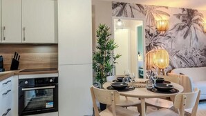 Une cuisine compacte dotée d’appareils électroménagers modernes, un coin repas avec une table ronde et des chaises, et un espace de vie avec un canapé et des œuvres d’art décoratives au mur.