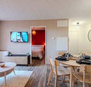 Une chambre d’hôtel moderne équipée d’un lit, d’un téléviseur fixé au mur, d’un coin repas avec une table et des chaises, et d’une petite kitchenette.