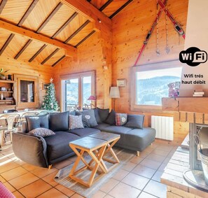 Ein gemütliches Holzhaus mit Sofa, Couchtisch und Blick auf die Berge.