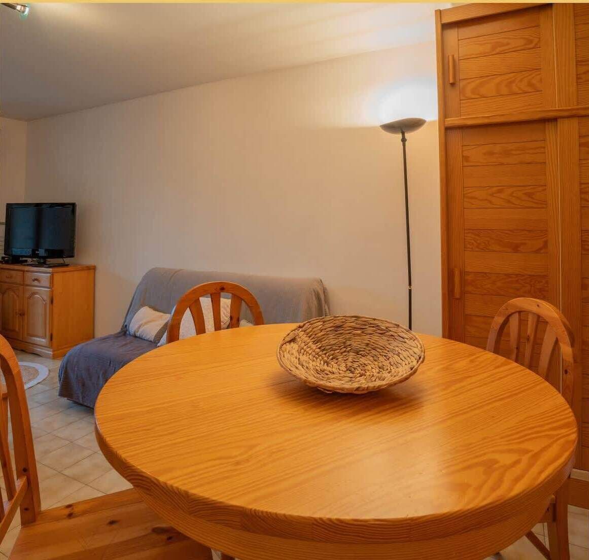A round wooden dining table with a woven basket in the center, surrounded by wooden chairs.