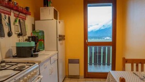Una cucina compatta con piano cottura a gas, forno, frigorifero e microonde. Una finestra si affaccia su un paesaggio innevato.