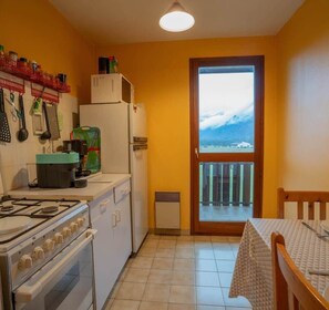 A compact kitchen with a gas stove, oven, refrigerator, and microwave. A window offers a view of a snowy landscape. - L'appartement des Cimes I Doussard (Doussard)