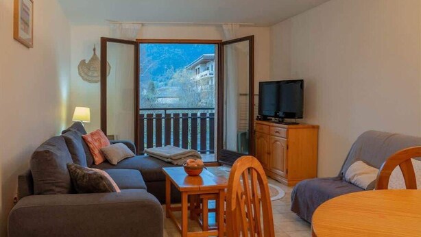 Un accogliente soggiorno con divano, tavolo da pranzo e TV. È presente un balcone con vista sulle montagne.