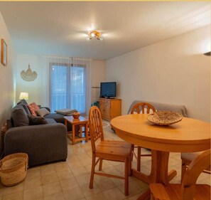 A cozy living room with a sofa, a dining table with chairs, a television, and a window with curtains. - L'appartement des Cimes I Doussard (Doussard)