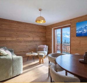 A cozy room with wooden walls, a dining table with chairs, a sofa, and a small round table with stools. - Le Balcon du Mont-Blanc I Duplex I Combloux (Combloux)